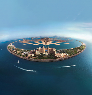 Panoramic view of Dubai's Business Bay area at twilight, with the city's architecture reflecting on the water surface and a bridge in the foreground.